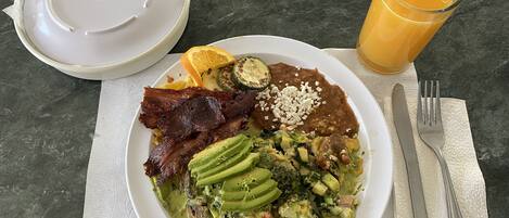 A plate of food with avocado, beans, and meat, a glass of orange juice, and a fork and knife on a table.