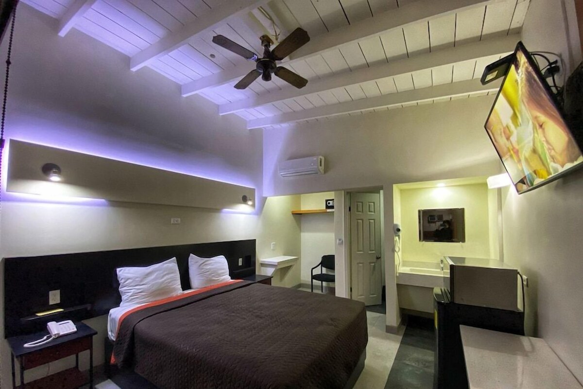 Una habitación de hotel con cama, escritorio, silla y un ventilador de techo.