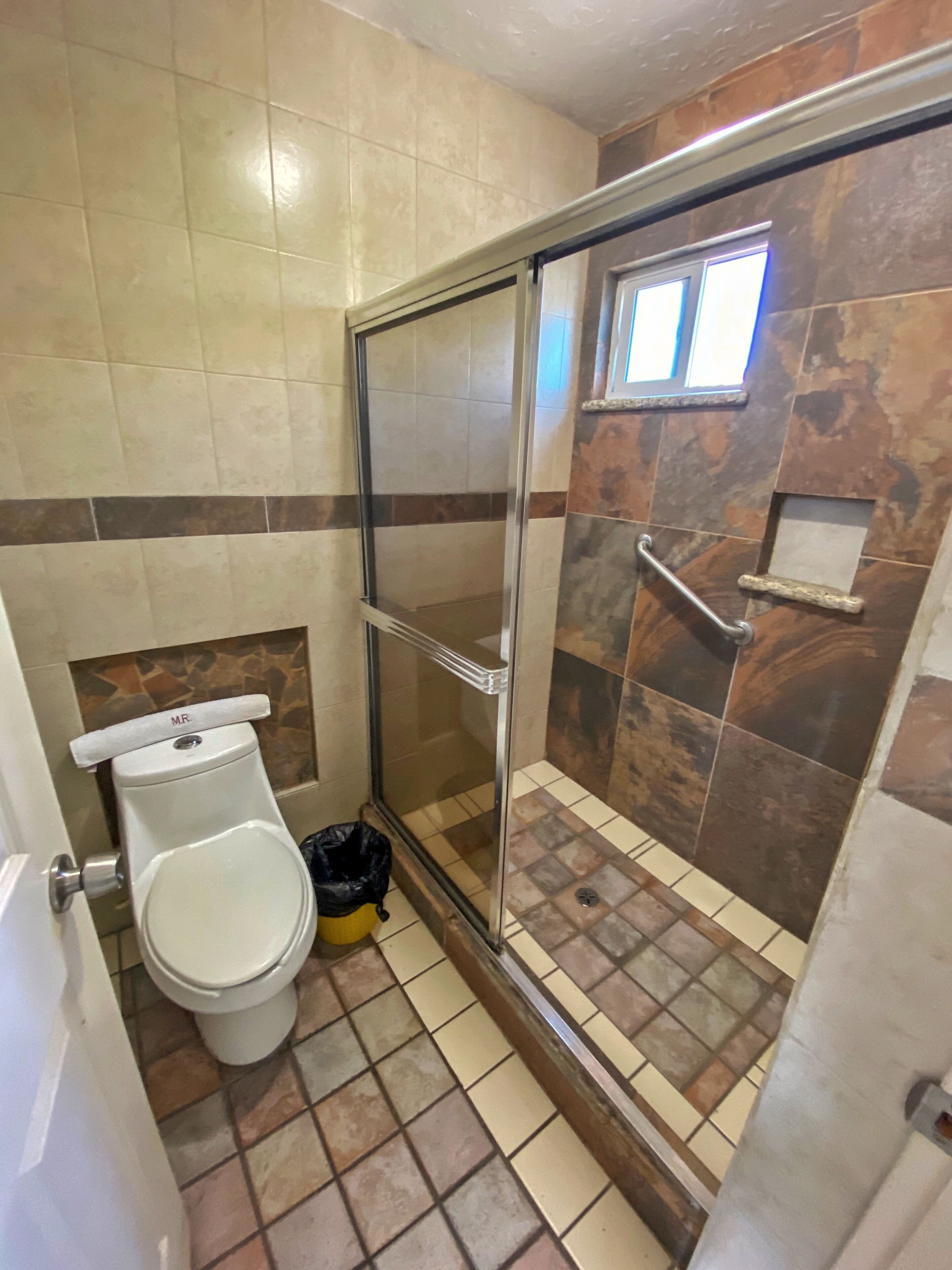 Une salle de bain avec des toilettes, une douche dotée d’une porte en verre et un sol carrelé.