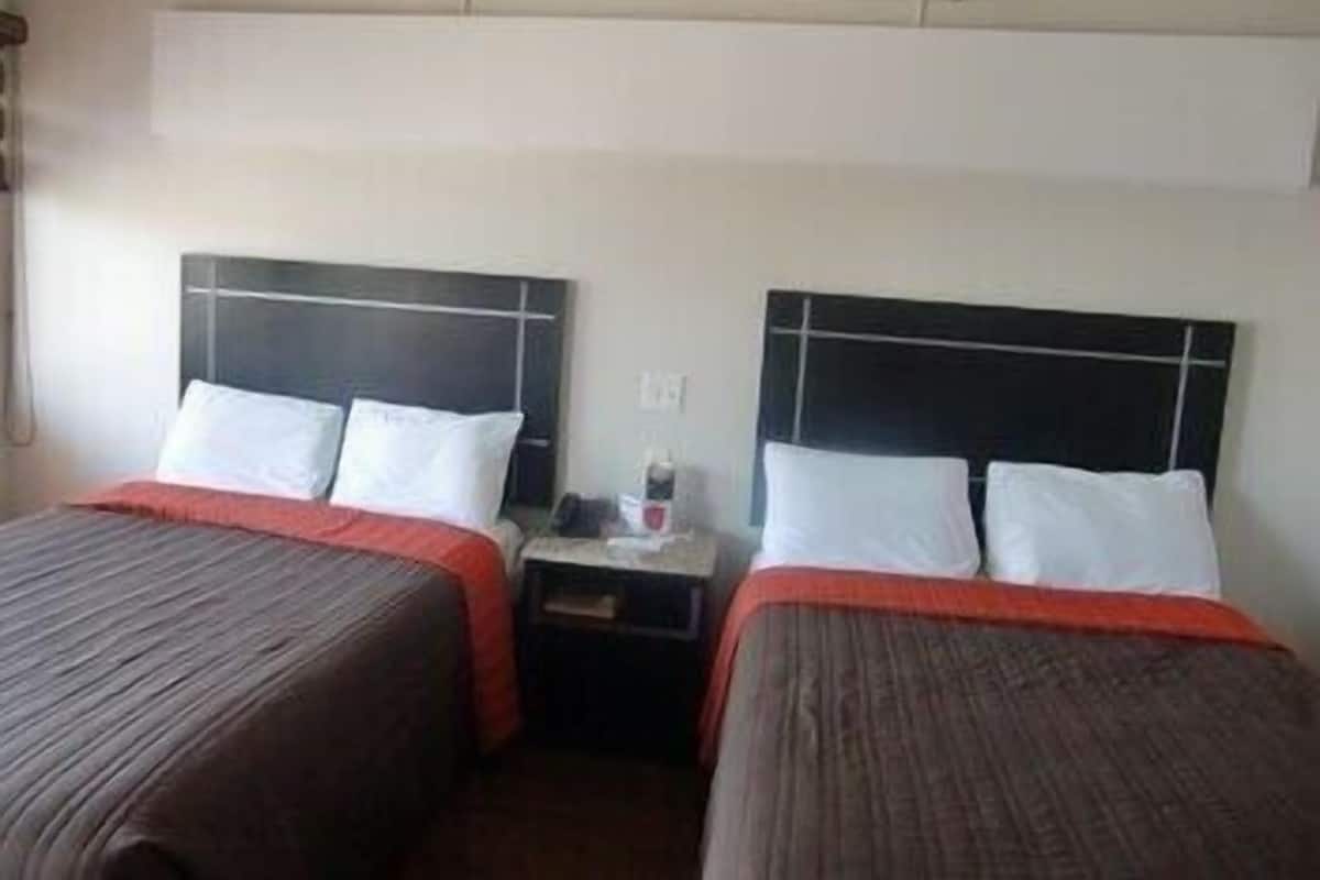 A hotel room with two beds, each with a headboard and pillows. There is a nightstand between the beds with a lamp and a small table.