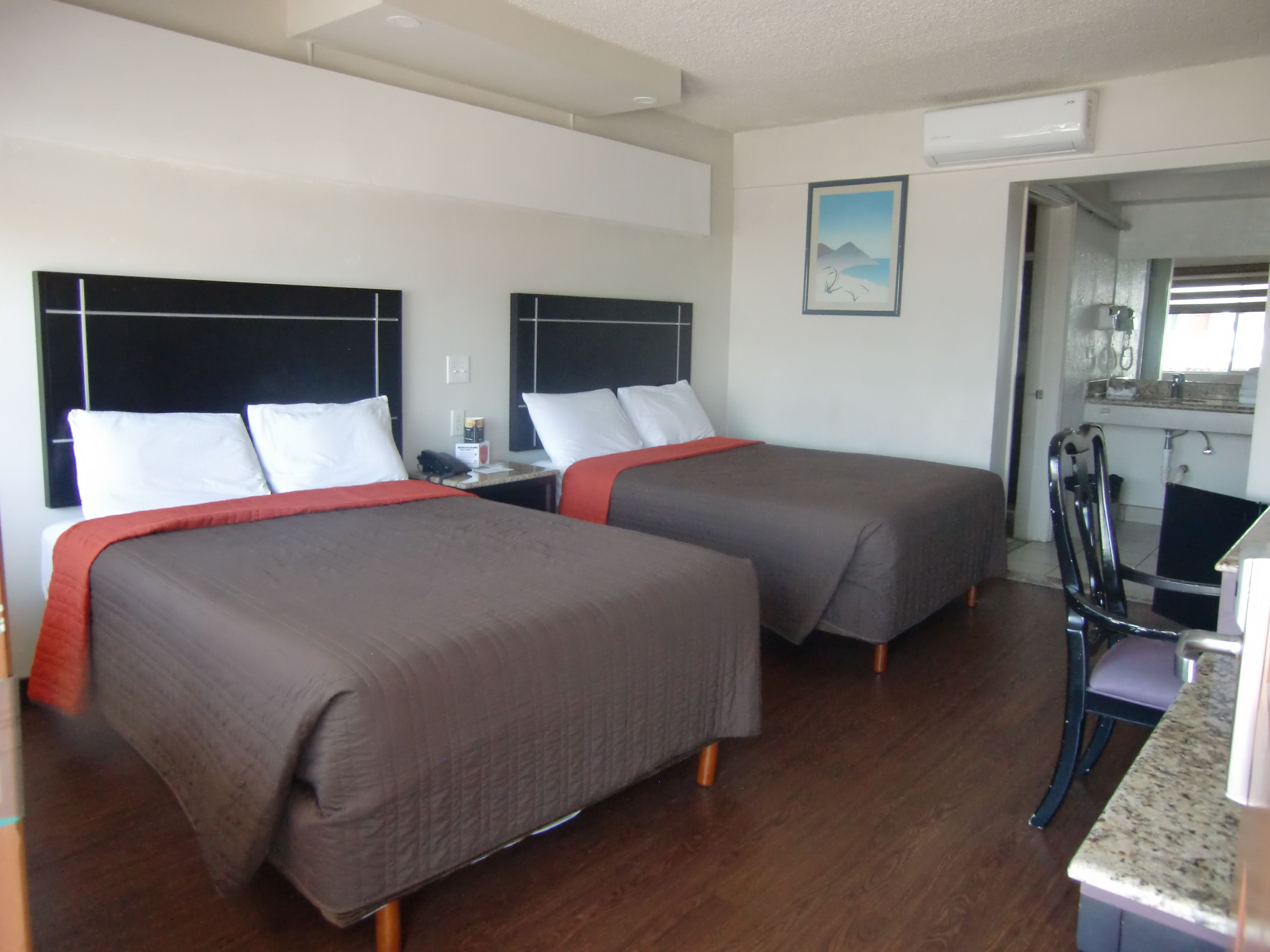 Een hotelkamer met twee bedden, een kleine tafel, een stoel en een kitchenette.