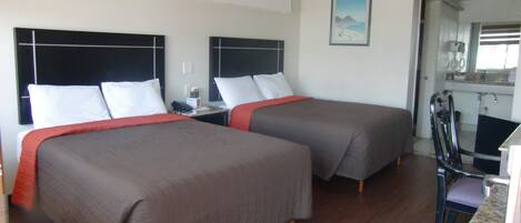 A hotel room with two beds, a small table, a chair, and a kitchenette.