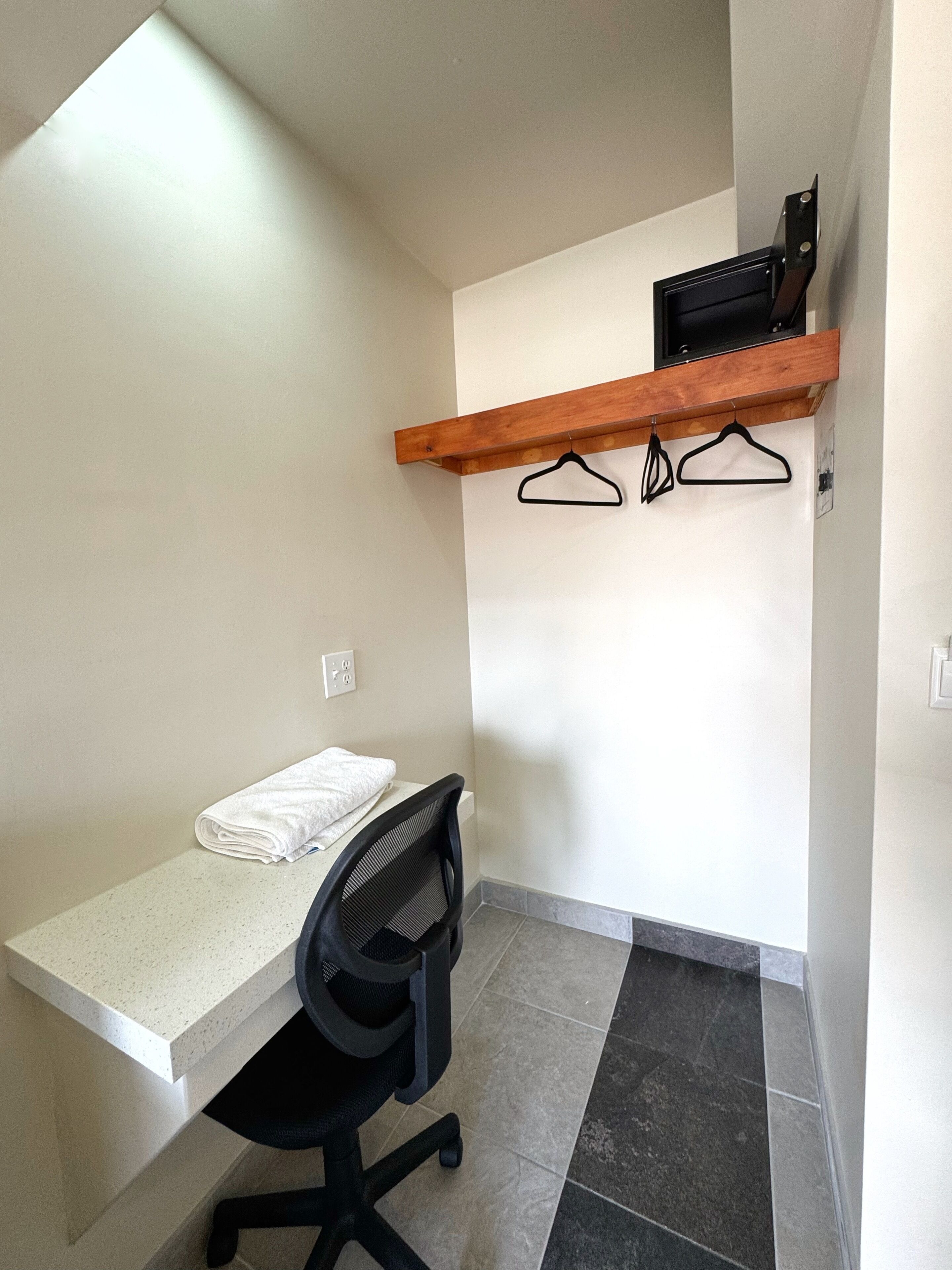 Um pequeno espaço de escritório com uma mesa, cadeira e uma prateleira de madeira com cabides.