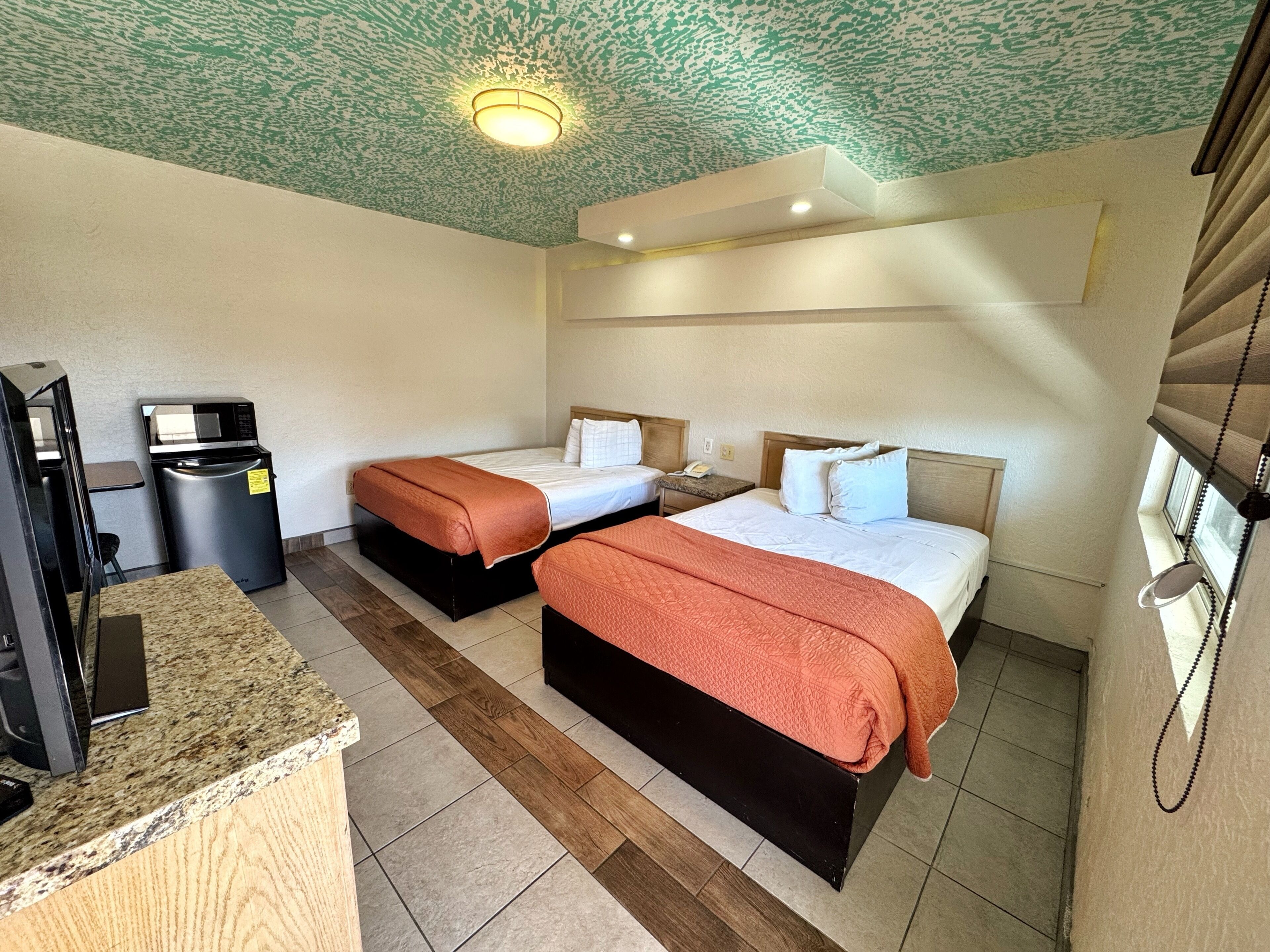 Een hotelkamer met twee bedden, een kitchenette, een afvalbak en een plafondlamp.
