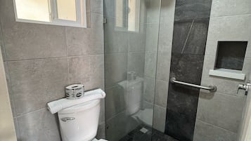 Un baño con inodoro, ducha y cabina de ducha con paredes de vidrio.