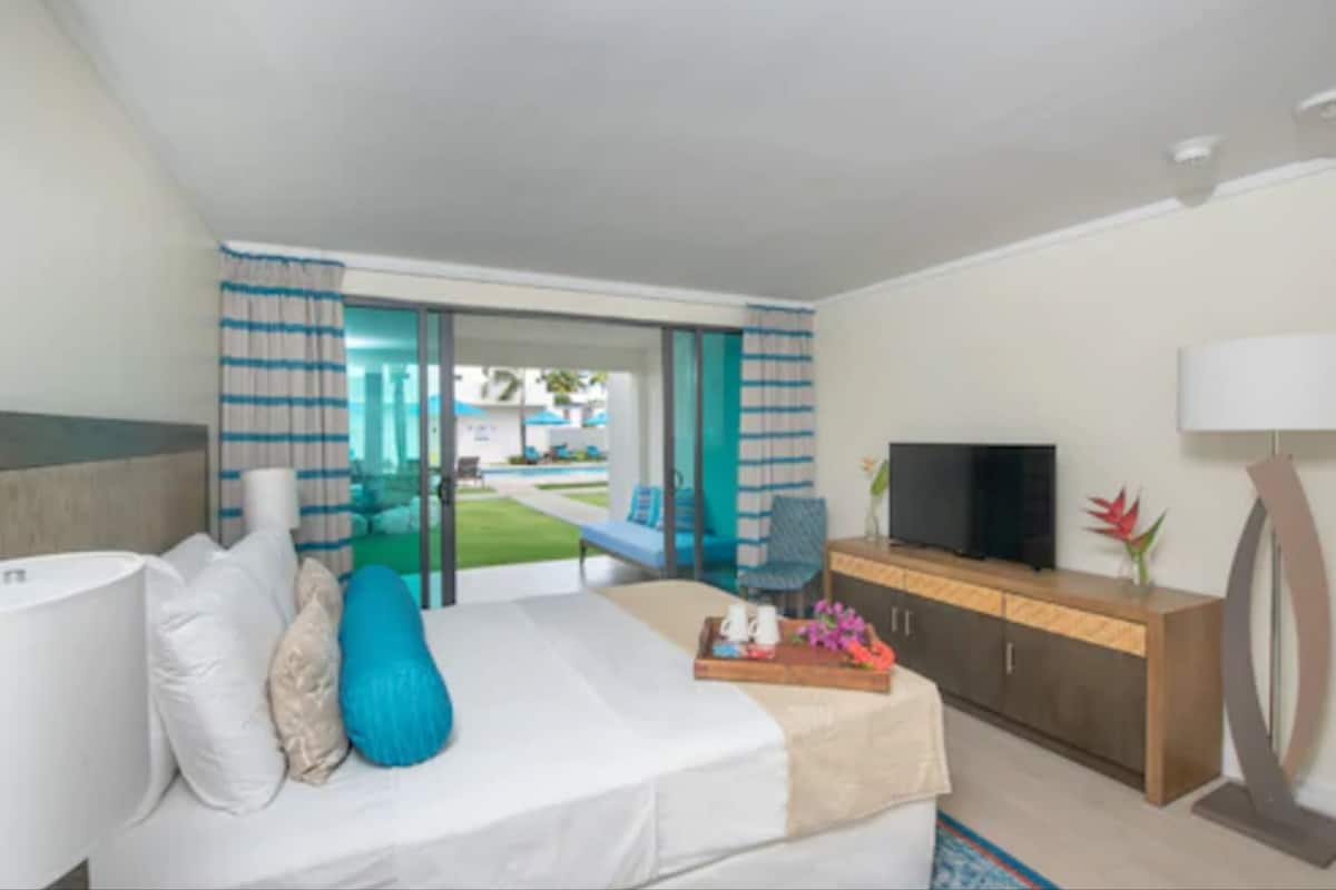 A hotel room with a bed, a TV, a desk, and a view of the outdoor area.