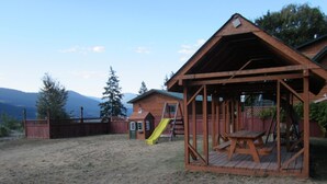A wooden playhouse with a slide and a picnic table in a backyard. - Jade Mountain Motel (Chase)