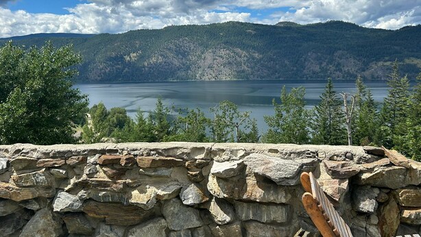A stone wall with a wooden ladder, overlooking a lake with mountains in the background. - Jade Mountain Motel (Chase)