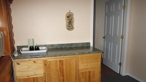 A kitchen with wooden cabinets, a granite countertop, and a wall-mounted spice rack. - Jade Mountain Motel (Chase)