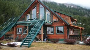 A log cabin with a steeply pitched roof, large windows, and a green staircase leading to a balcony. - Jade Mountain Motel (Chase)