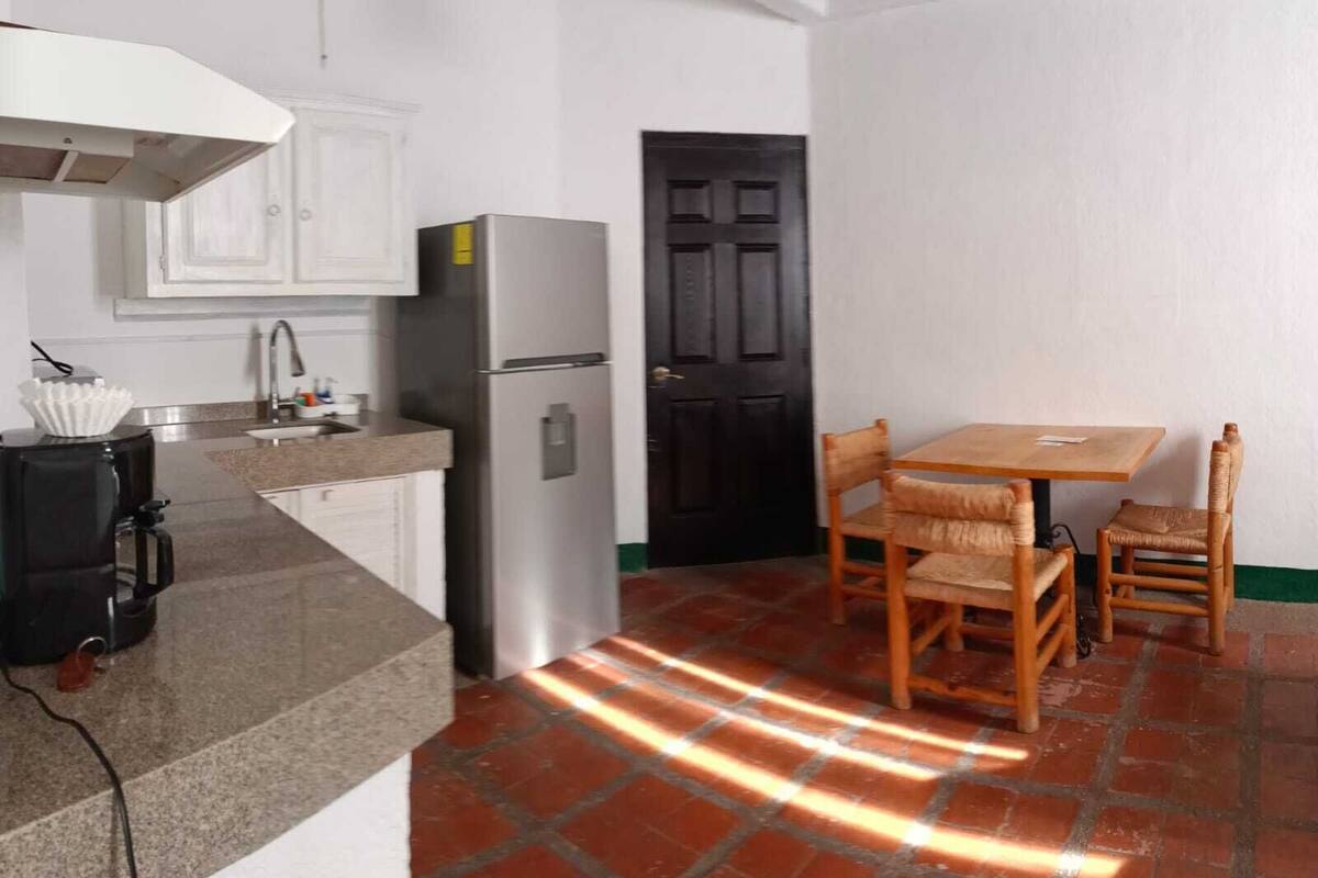 A compact kitchen with white cabinets, a stainless steel refrigerator, a coffee maker, and a dining table with two chairs.