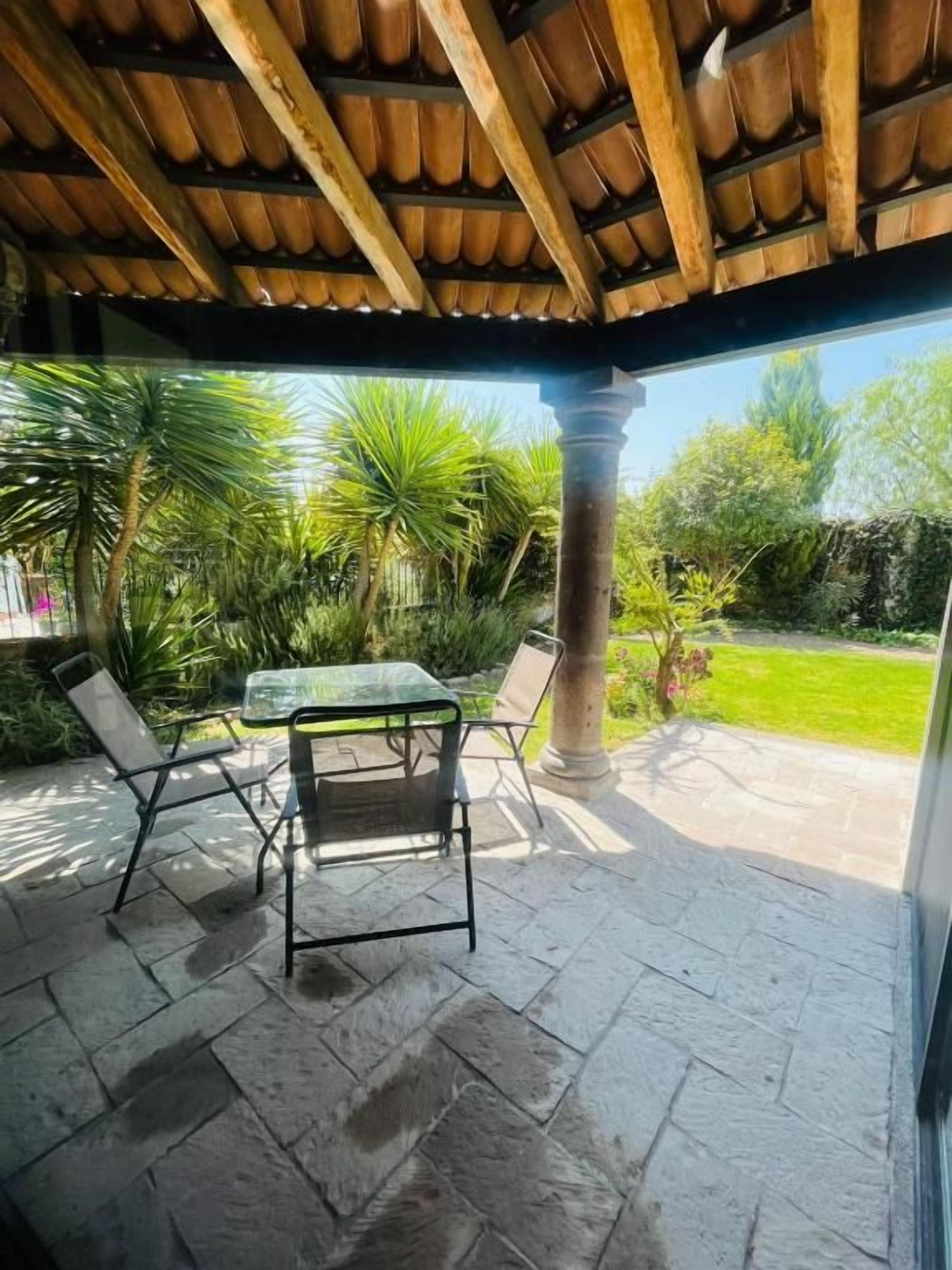 Un patio al aire libre con suelo de piedra, una mesa de vidrio y sillas de metal.