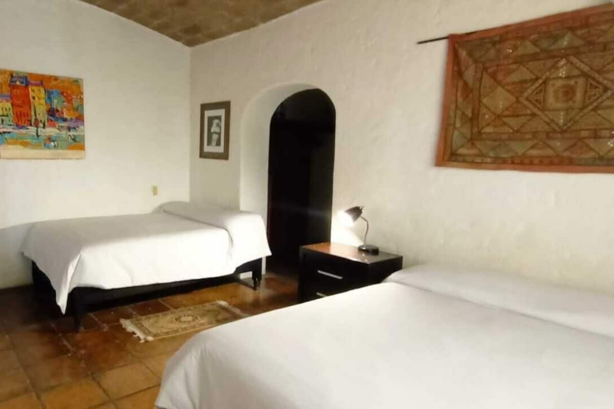 A bedroom with two beds, a sofa, a nightstand, and a painting on the wall.