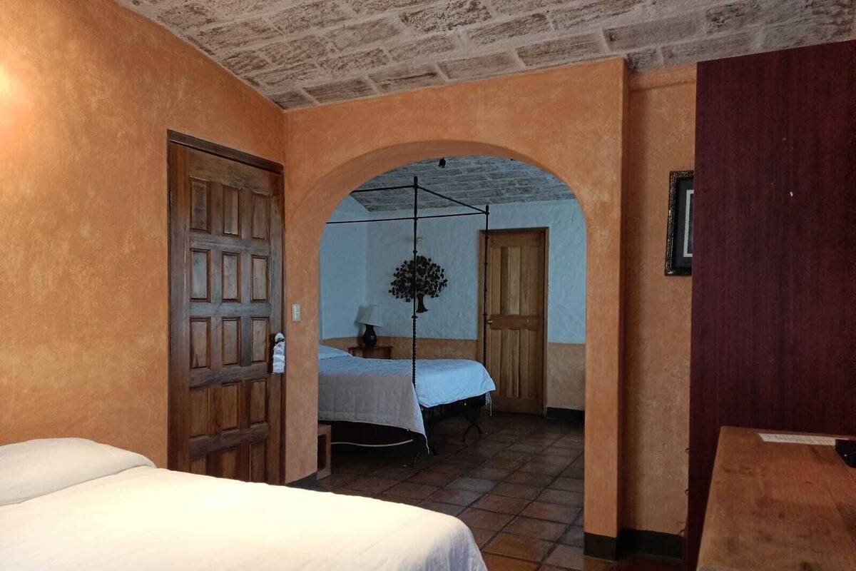 A room with a bed, a wooden door, a small table, and a hanging light fixture.