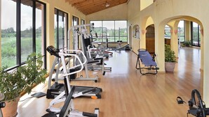 A spacious gym with exercise equipment, large windows, and a wooden floor.