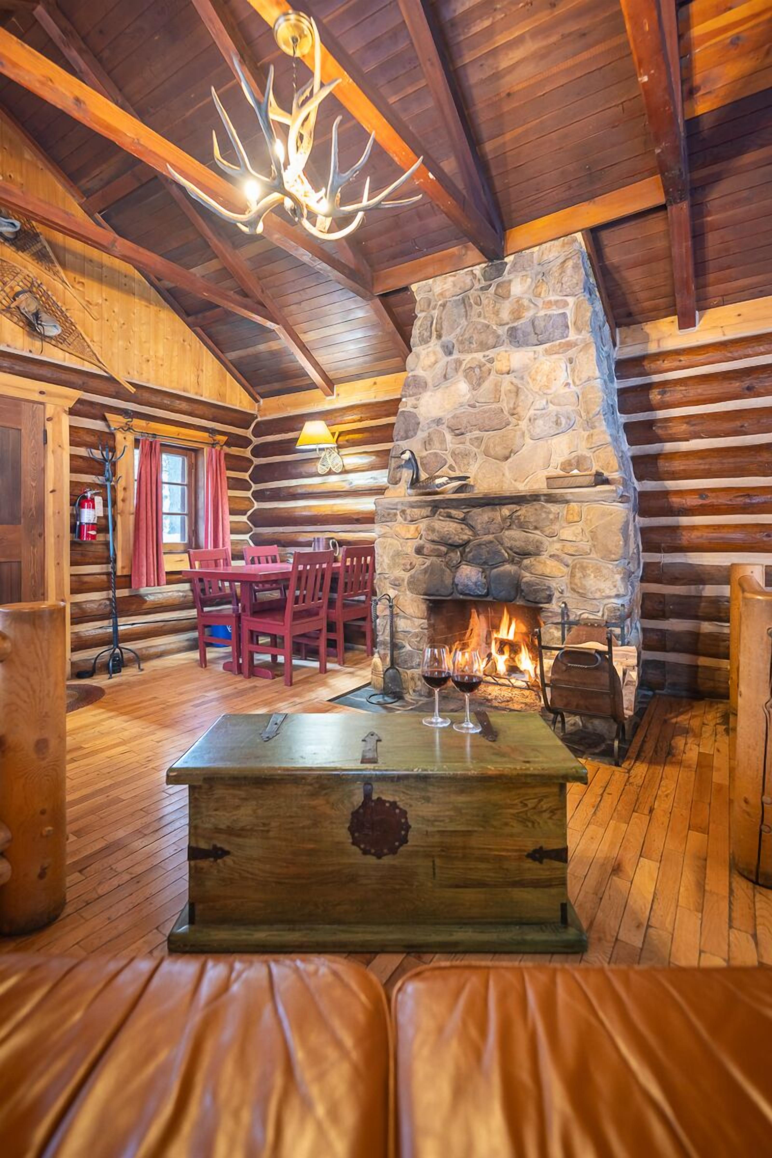 L’intérieur d’une cabane en rondins, avec une cheminée en pierre, des meubles en bois et un canapé en cuir.