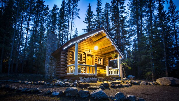 A log cabin with a porch and stone chimney, surrounded by a forest. - Storm Mountain Lodge Cabins & Dining (Castle Junction)