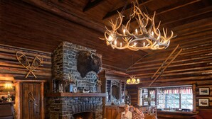 A cozy log cabin interior with a stone fireplace, leather furniture, and a chandelier made from antlers. - Storm Mountain Lodge Cabins & Dining (Castle Junction)