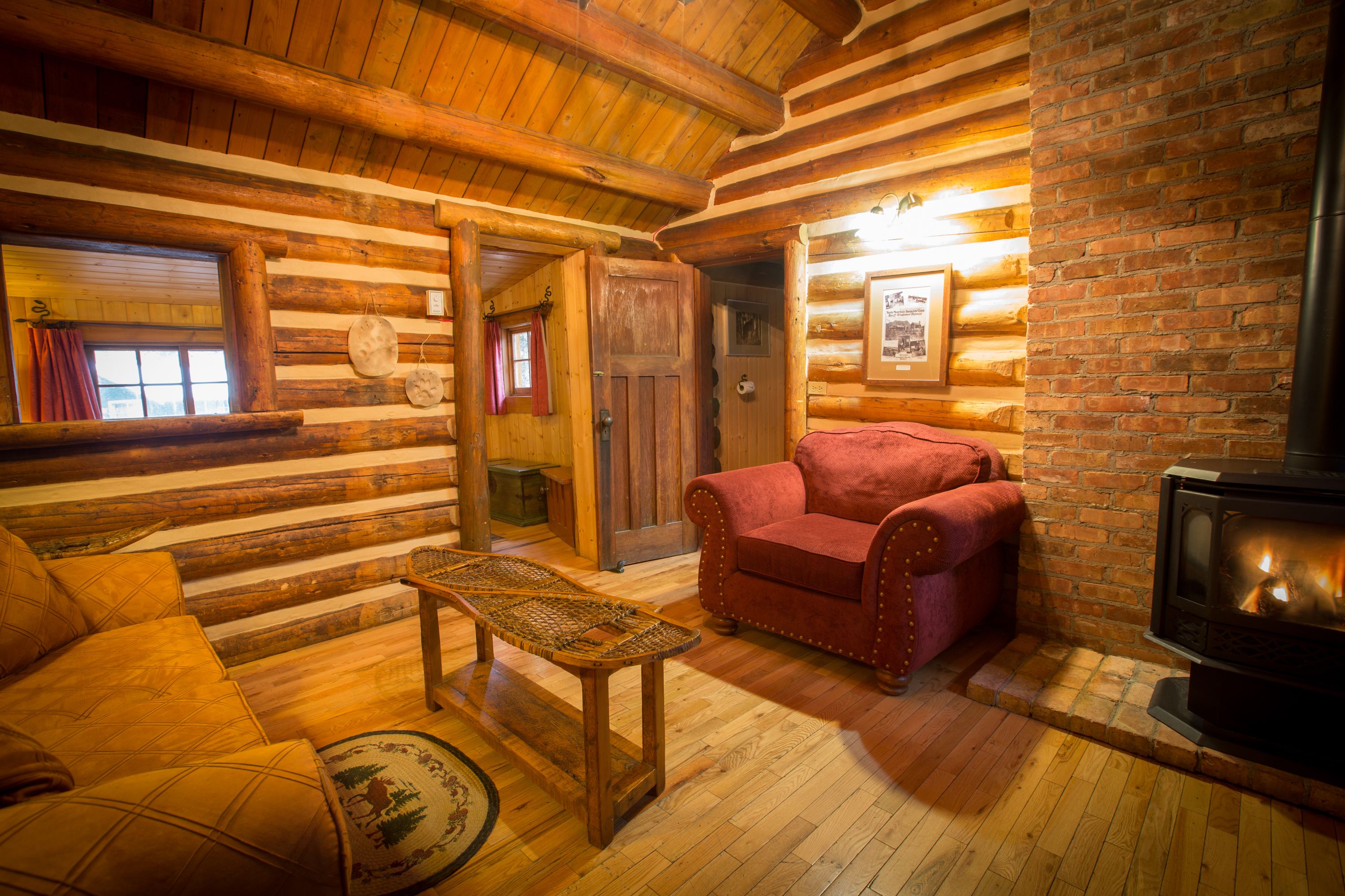 A cozy log cabin interior with a fireplace, wooden furniture, and a brick wall.