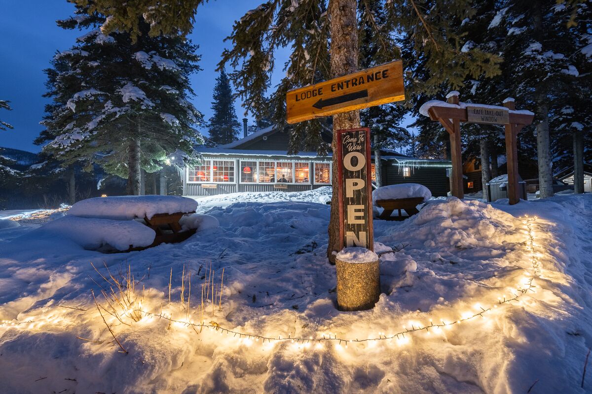 Entrada d'una cabana coberta de neu amb un senyal que indica el camí cap a l'allotjament.
