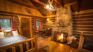 A cozy cabin interior with a stone fireplace, wooden furniture, and a bed with a quilt. - Storm Mountain Lodge Cabins & Dining (Castle Junction)