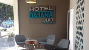 Un vestíbulo de hotel con un letrero que dice "HOTEL DAJANA BLVD". Hay varias sillas y una mesa redonda pequeña.