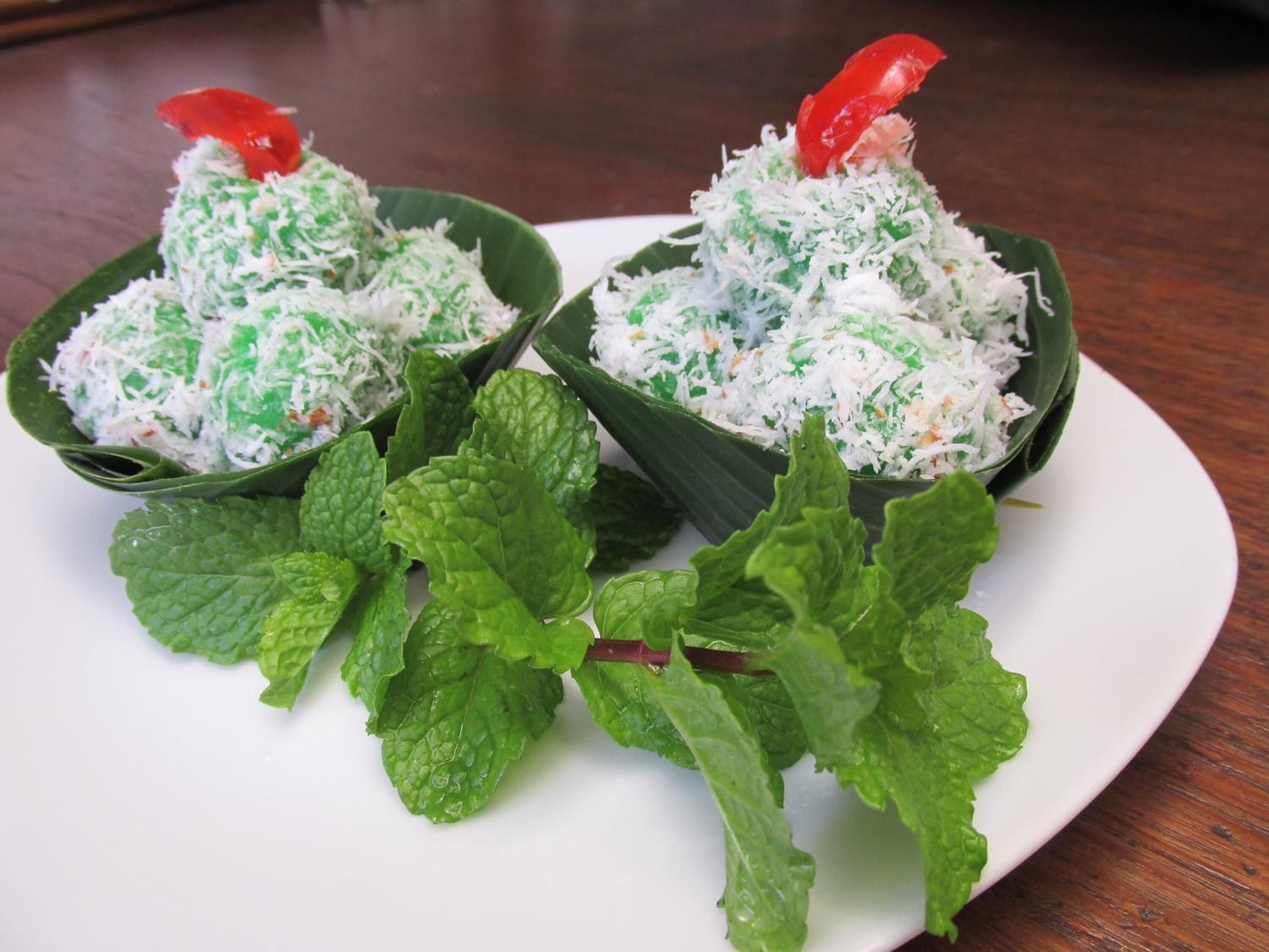 Deux bols de nourriture, garnis de noix de coco râpée et de feuilles de menthe, sont présentés sur une assiette.