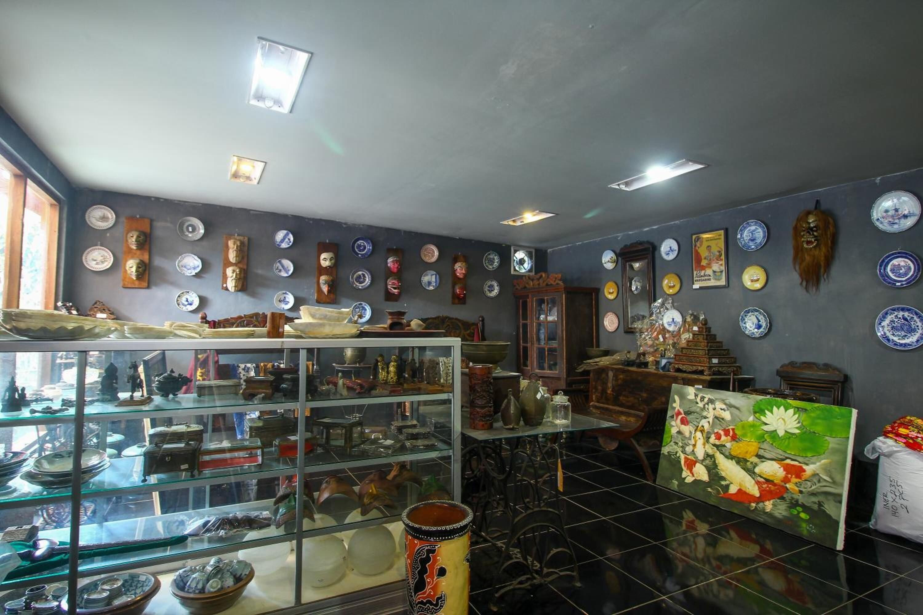 A room with a glass display case filled with various pottery and ceramics, a painting of koi fish, and a collection of plates and bowls on the walls.