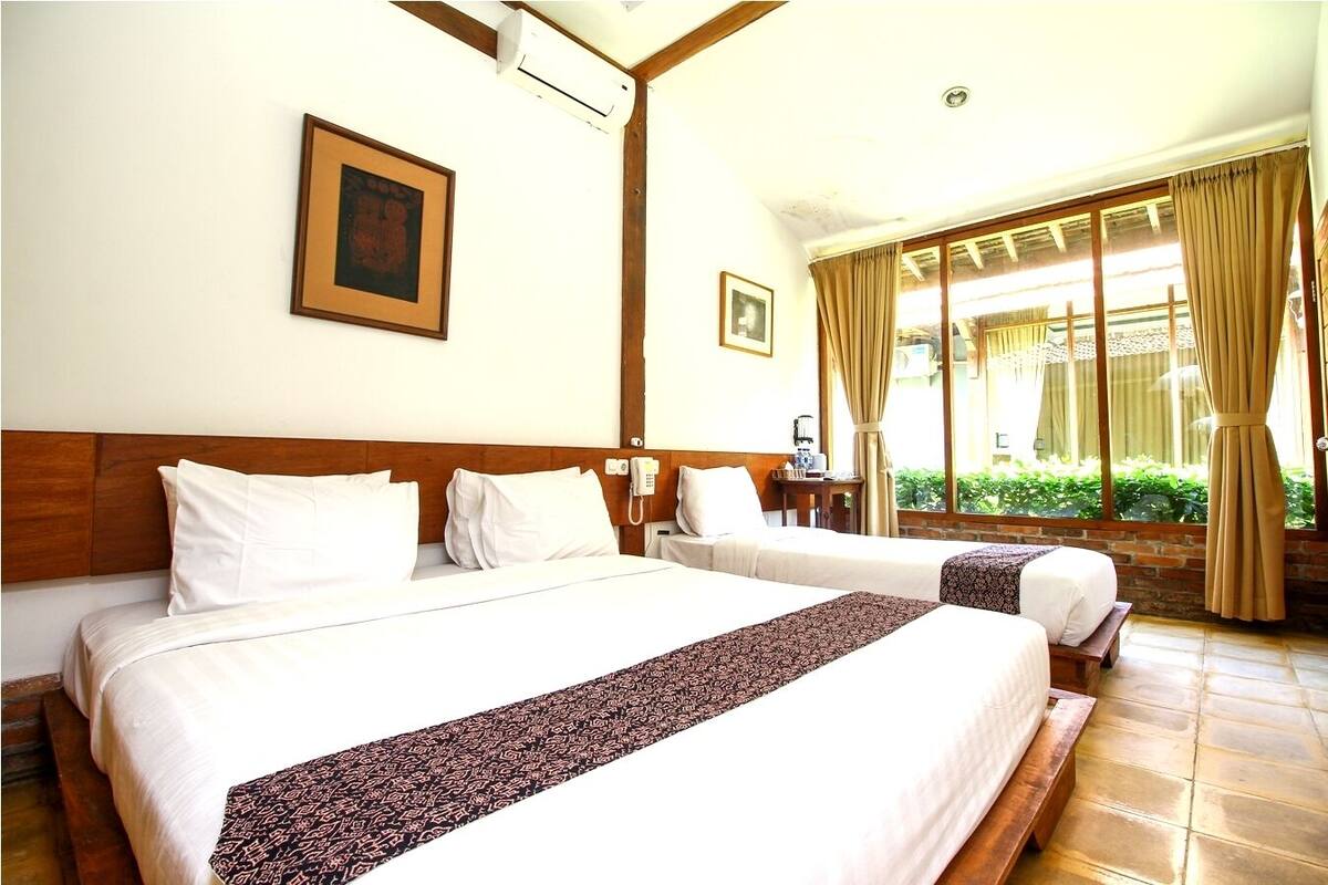 Habitación de hotel con dos camas, cabecero de madera, teléfono y ventana con cortinas.