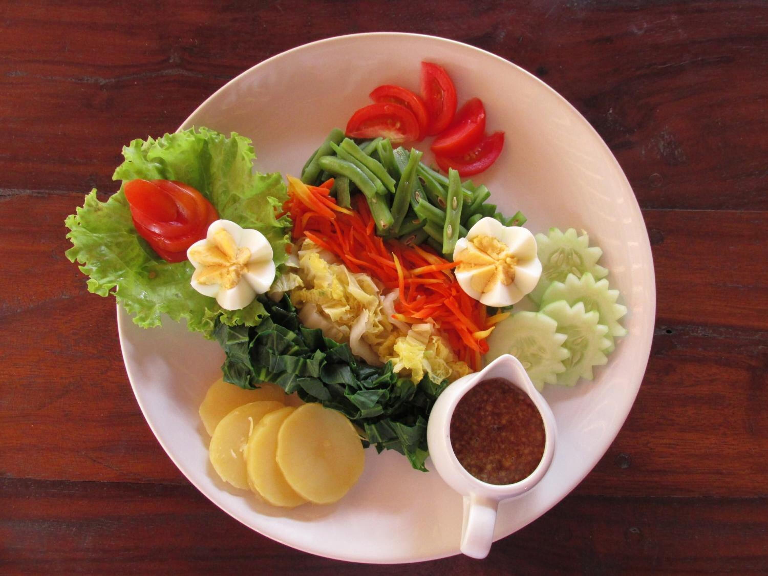 A plate of food with various vegetables, boiled eggs, and a small cup of sauce.