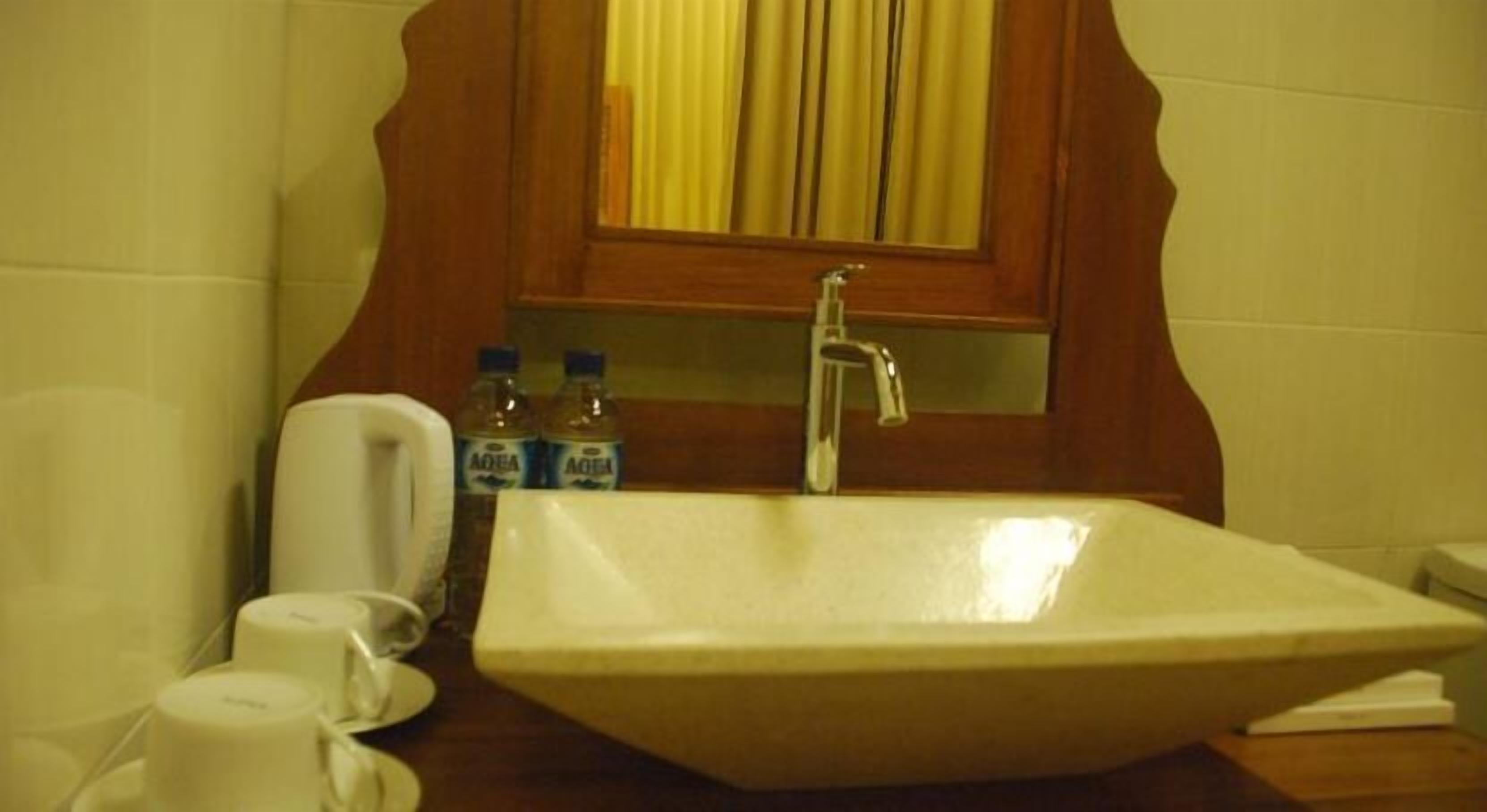 A bathroom with a large white sink, a mirror with a wooden frame, and two bottles of water on the counter.