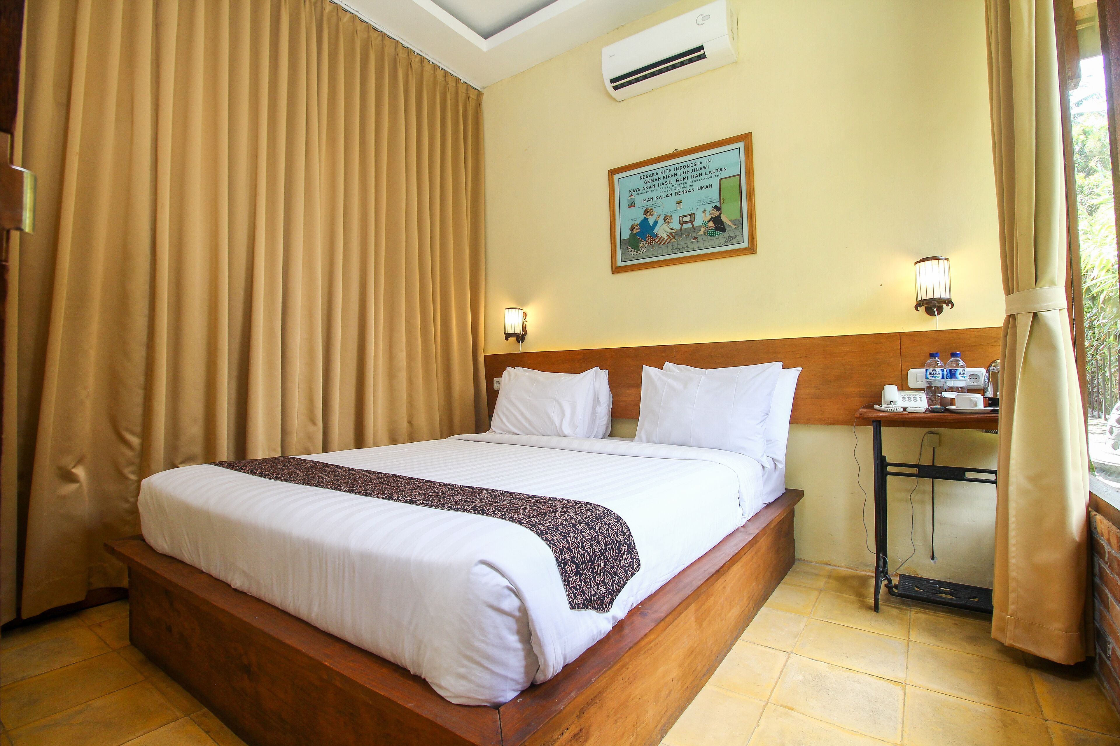 A hotel room with a large bed, a bedside table with a lamp, an air conditioner, and a wall-mounted picture.