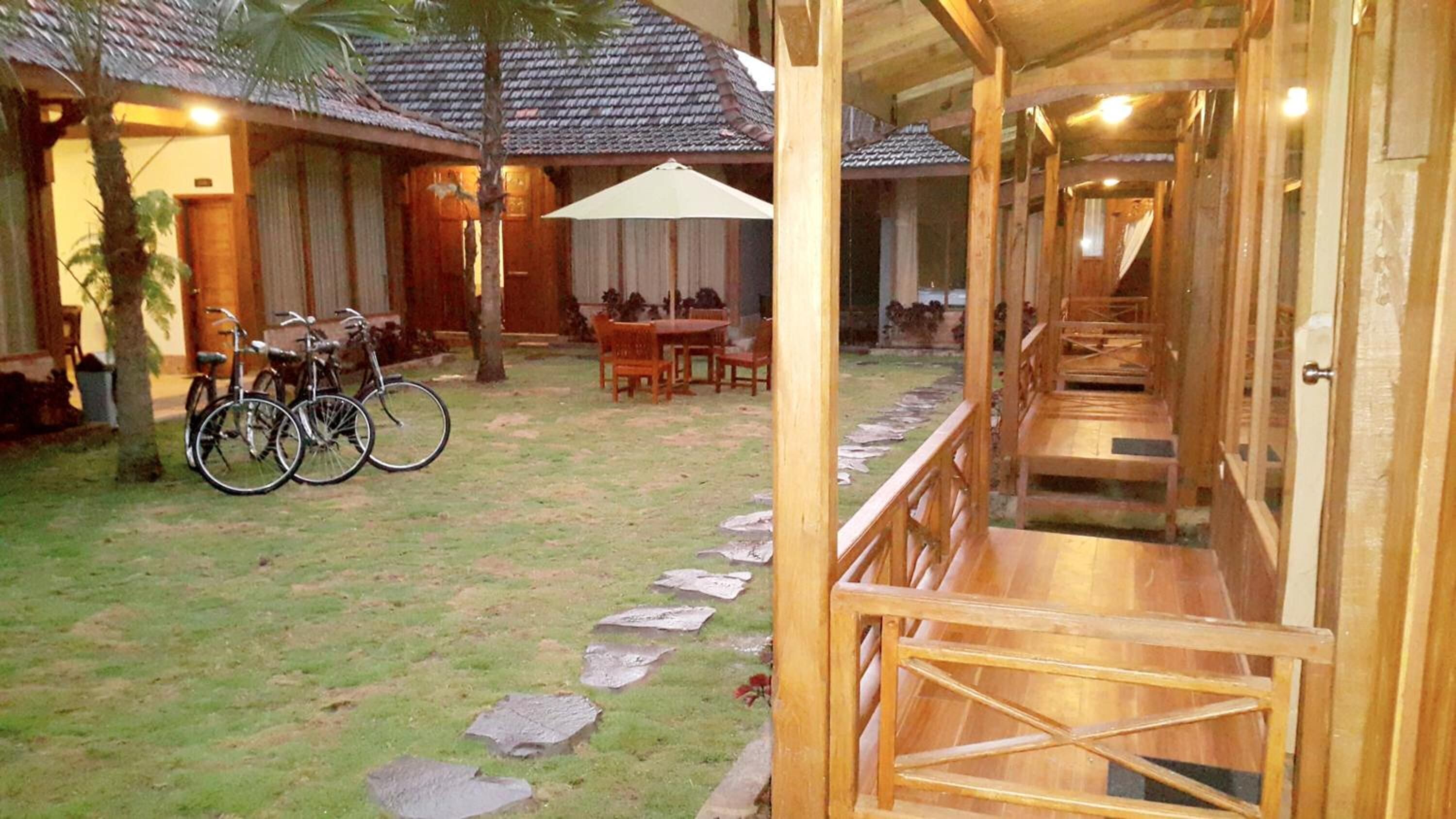 A wooden outdoor area with a stone path leading to a covered seating area. There are bicycles parked and a table with chairs.