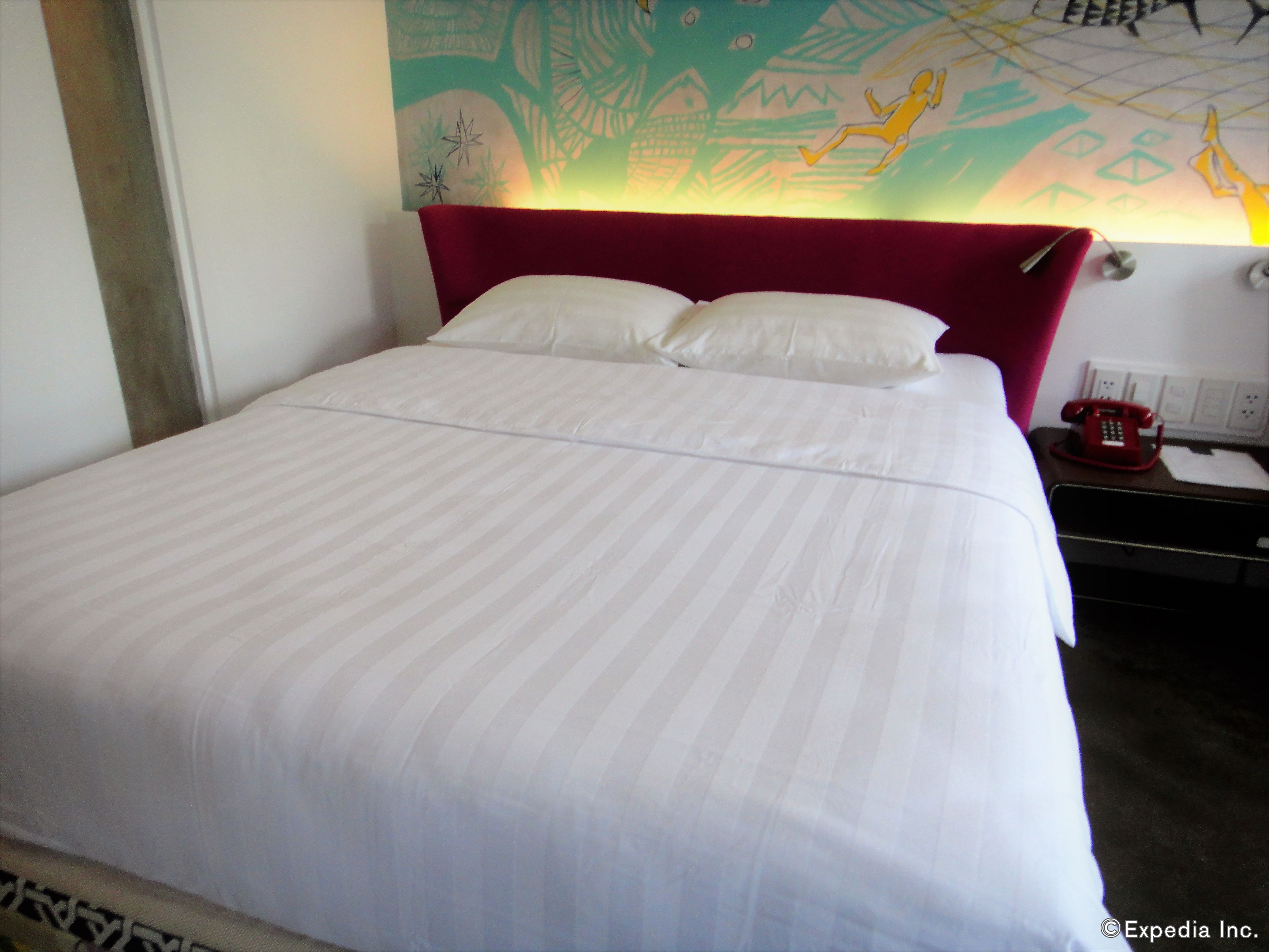 A bed with white bedding, a red headboard, and a wall mural.