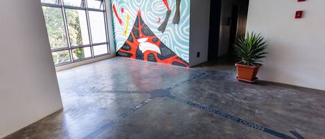 A spacious hallway with directional arrows on the floor, a mural with abstract designs, and a potted plant.