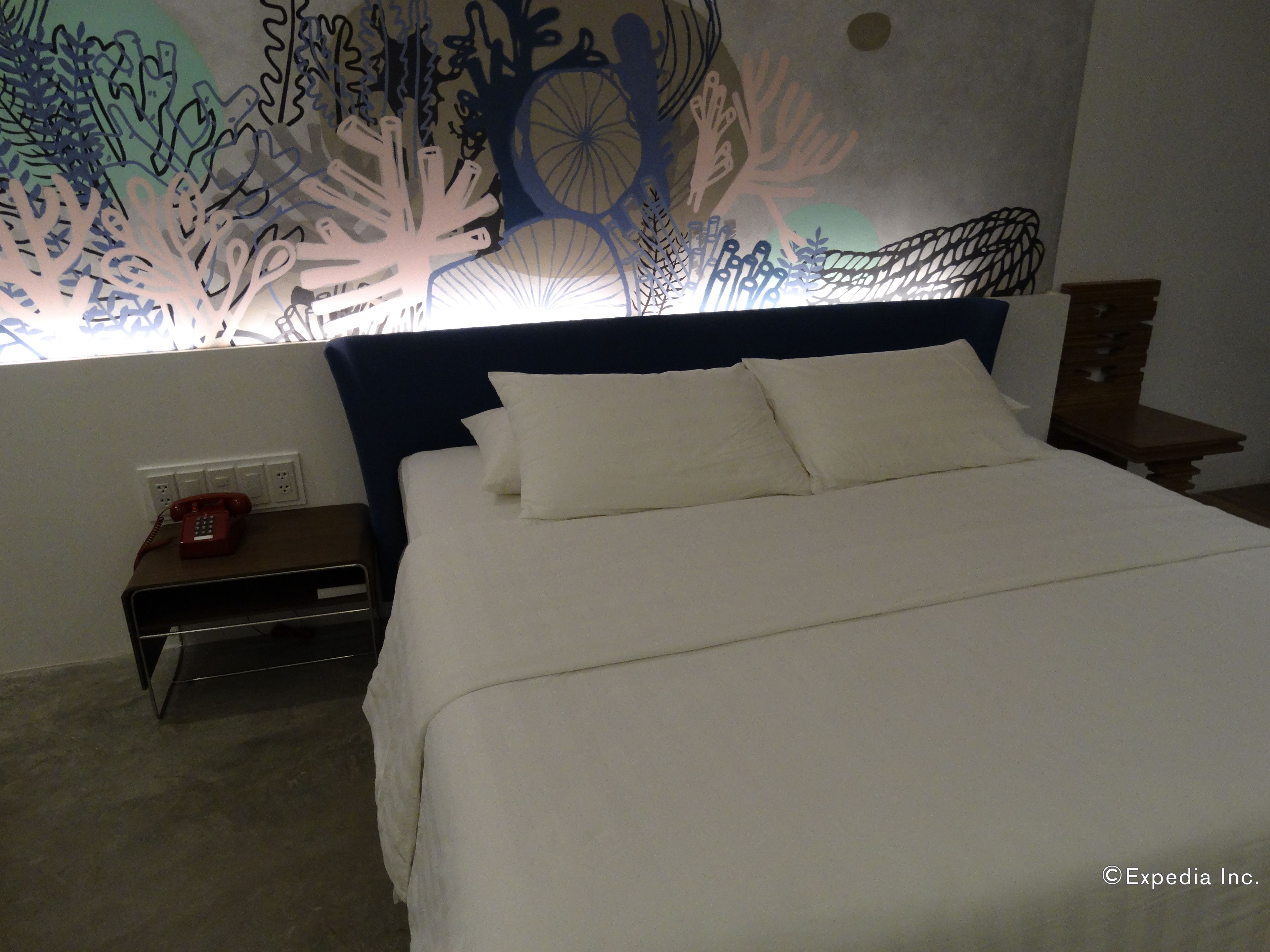 Quarto de hotel com cama, mesa de cabeceira, telefone e parede com padrão decorativo.