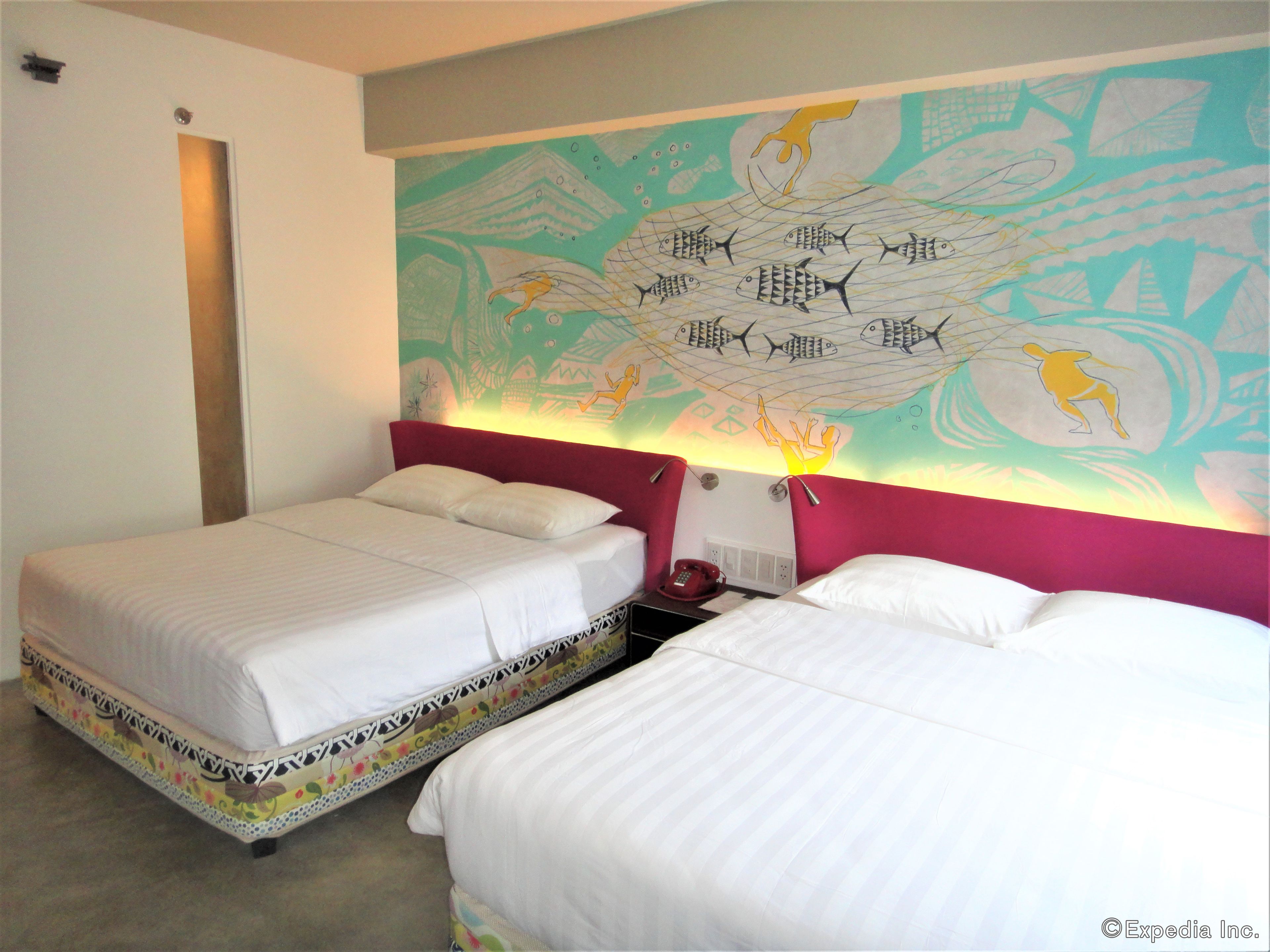 A hotel room with two beds, a colorful mural on the wall, and a red headboard.