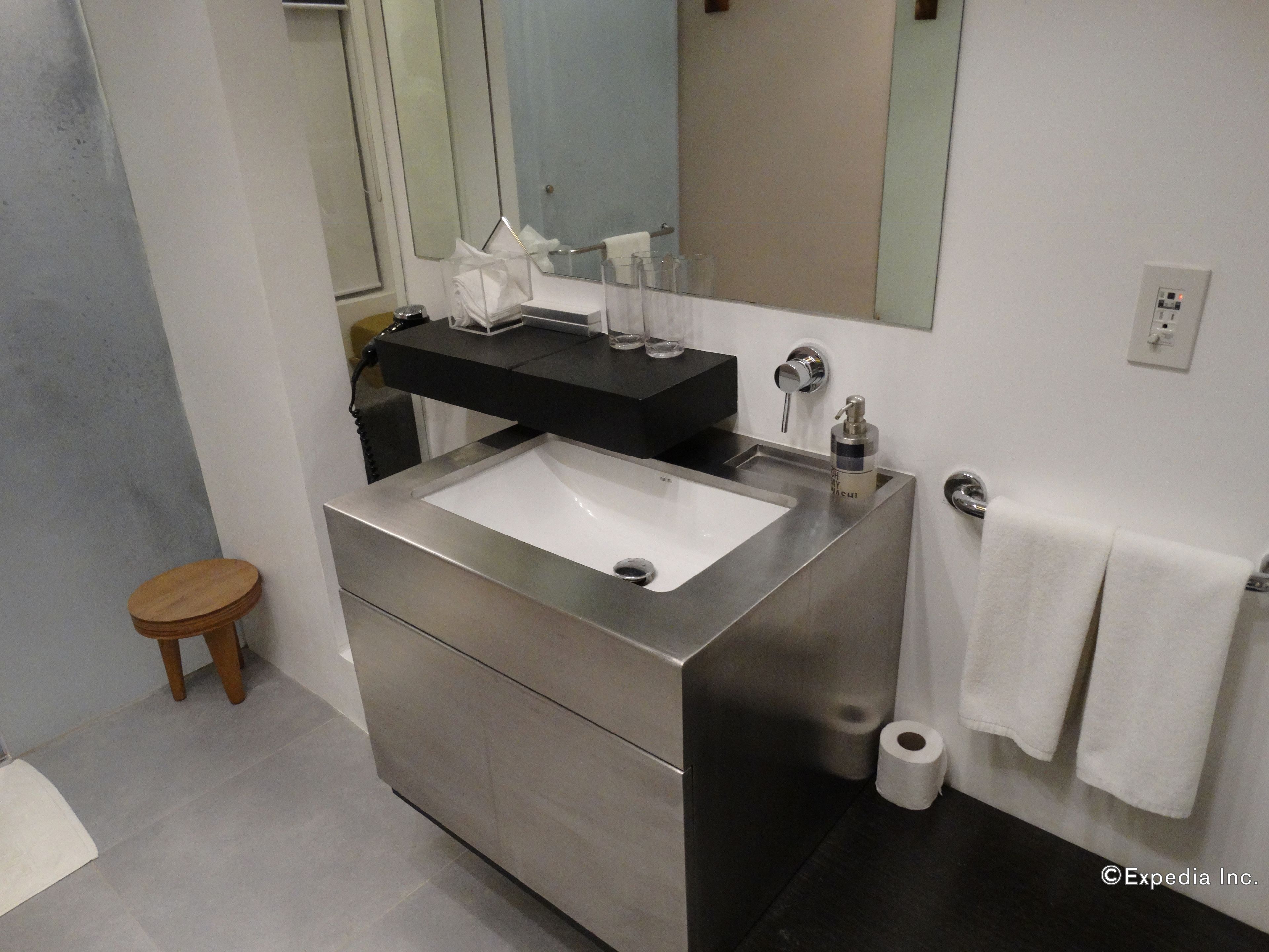 A modern bathroom with a stainless steel sink, a black countertop, a mirror, and a wooden stool.