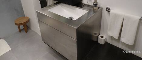 A modern bathroom with a stainless steel sink, a black countertop, a mirror, and a wooden stool.