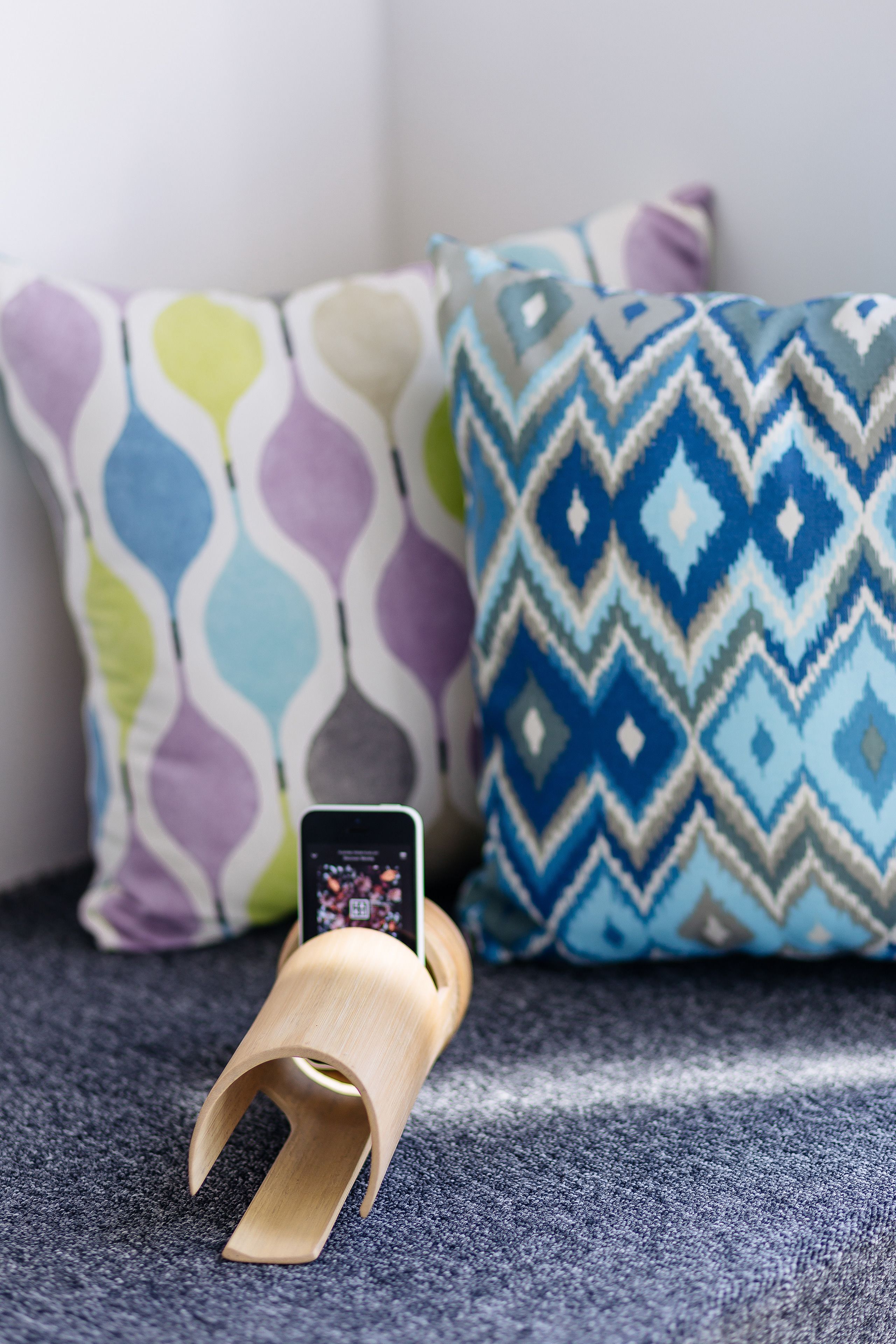 Un teléfono inteligente sobre un soporte de madera con un cojín estampado al fondo.