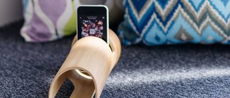 Un teléfono inteligente sobre un soporte de madera con un cojín estampado al fondo.