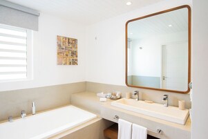 A modern bathroom with a large mirror, a bathtub, and a vanity with a sink.