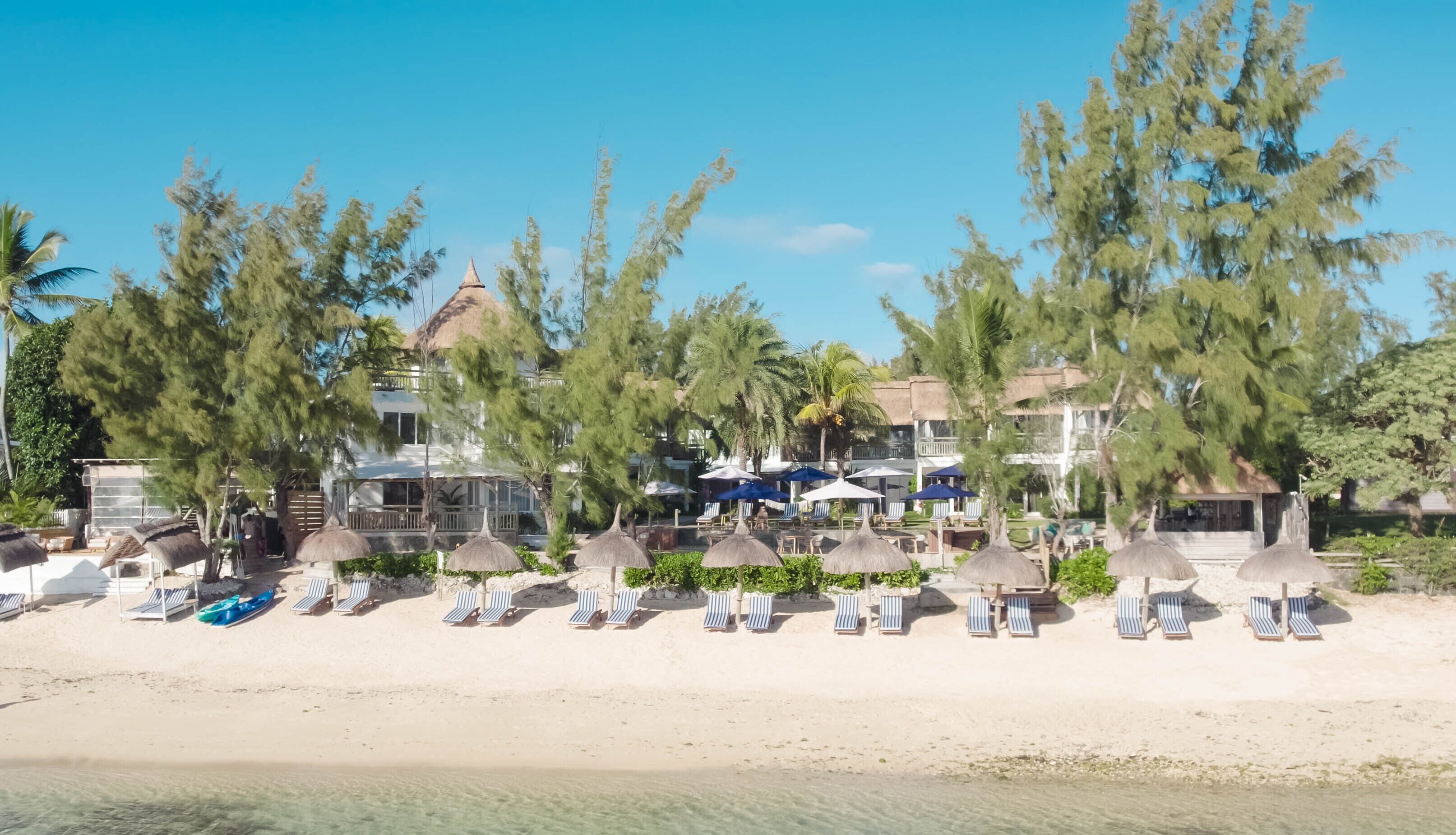 Un resort en la playa con sillas de descanso y sombrillas, una piscina y un edificio con varios balcones.