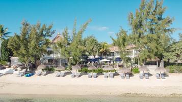 Un resort en la playa con sillas de descanso y sombrillas, una piscina y un edificio con varios balcones.