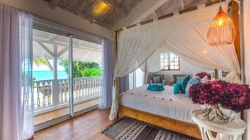 A bedroom with a large bed, a balcony with a view of the ocean, and a hanging light fixture.