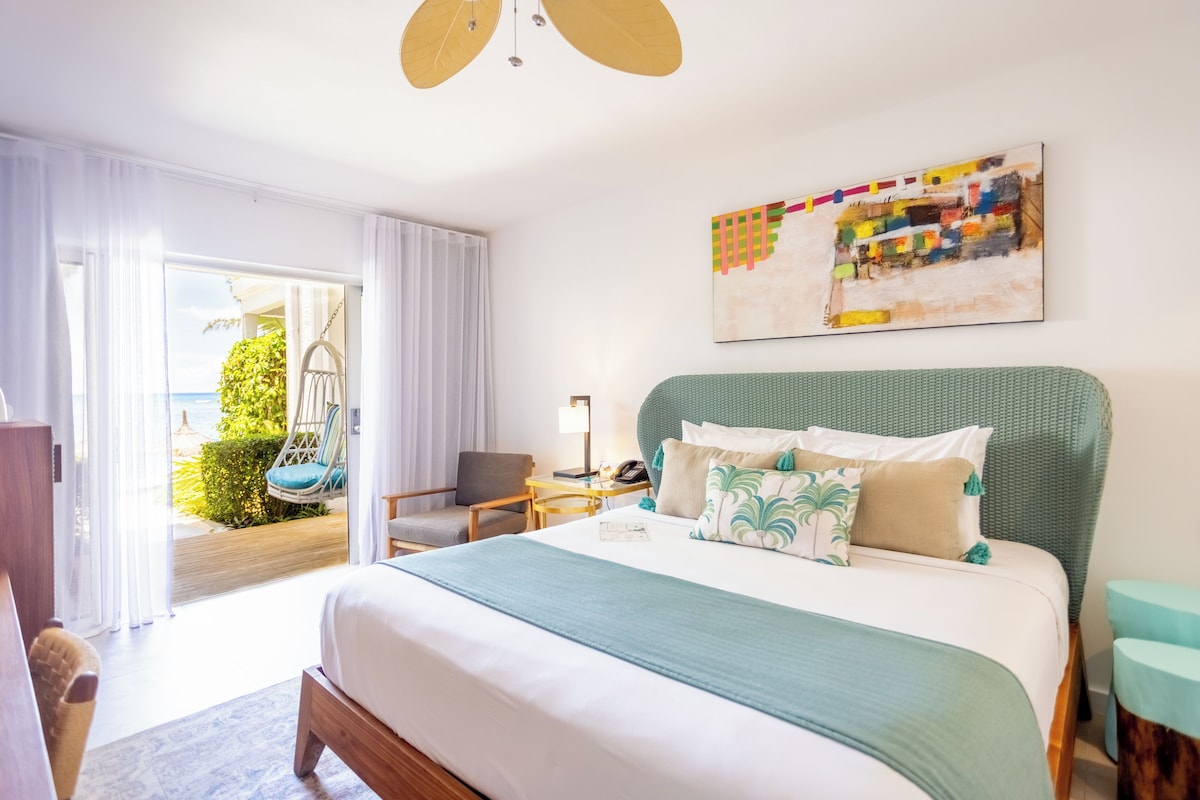 Une chambre d’hôtel avec un grand lit, une vue sur l’extérieur, un fauteuil suspendu et un tableau au mur.
