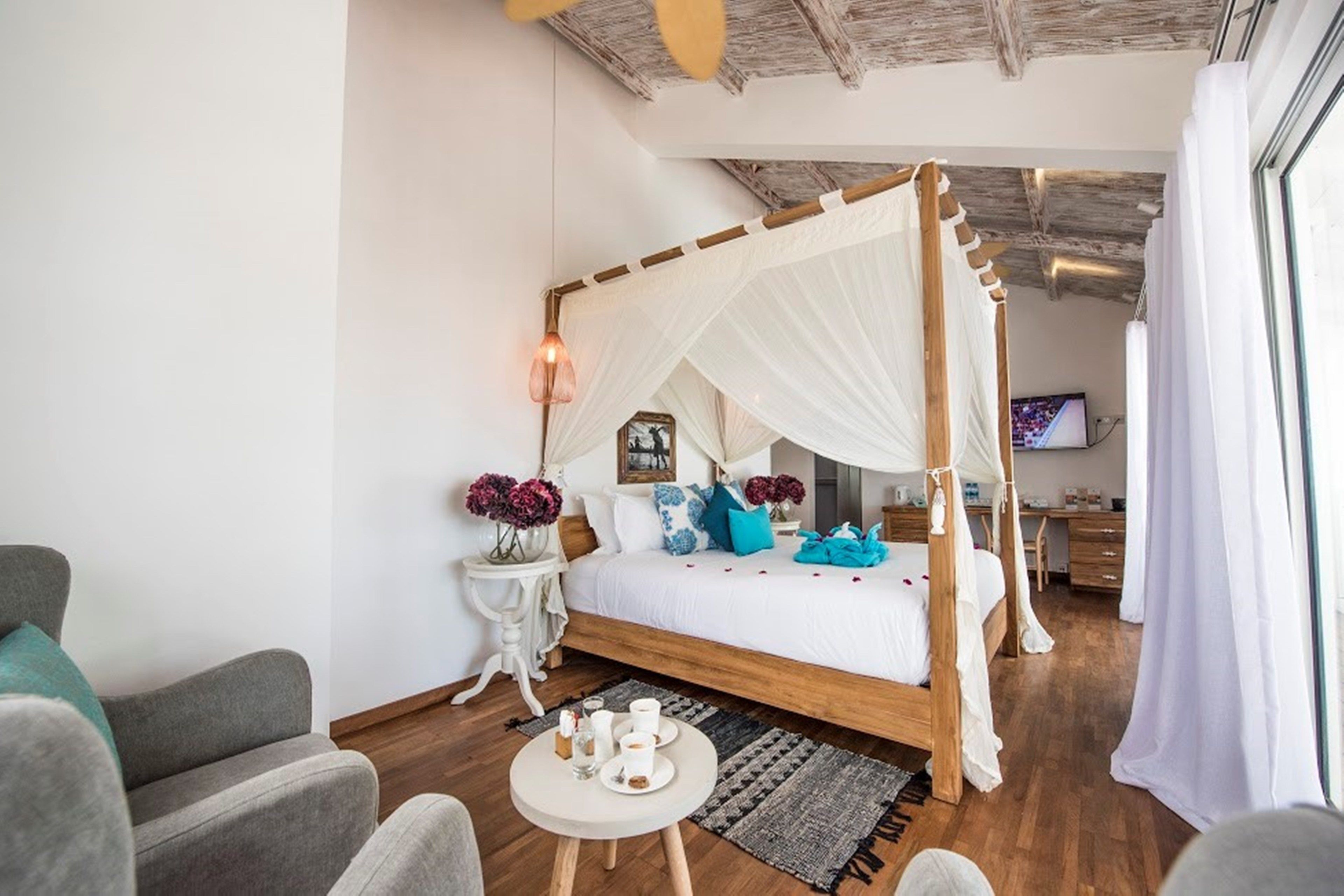 Un dormitorio con cama con dosel, una mesita redonda con una bandeja de objetos, un televisor y un escritorio con una silla.
