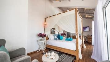 Un dormitorio con cama con dosel, una mesita redonda con una bandeja de objetos, un televisor y un escritorio con una silla.