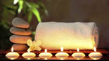 Una pila de piedras lisas, una toalla blanca y velas encendidas sobre una superficie de madera.