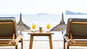 Een houten terras met twee ligstoelen en een tafel met twee glazen jus d'orange.